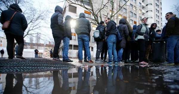 Migrants are reflected in a puddle as they queue in front of the compound of the Berlin Office of Health and Social Affairs (LAGESO) for their registration process, early morning in Berlin, Germany, February 2, 2016.