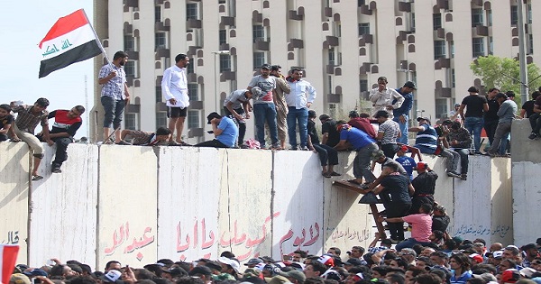 Iraqi protesters climb over a concrete wall surrounding the parliament after breaking into Baghdad's heavily fortified 