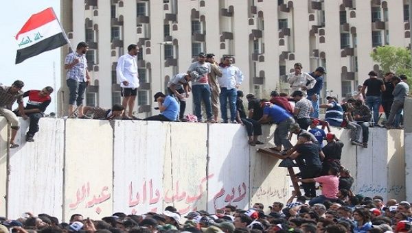 Iraqi protesters climb over a concrete wall surrounding the parliament after breaking into Baghdad's heavily fortified 