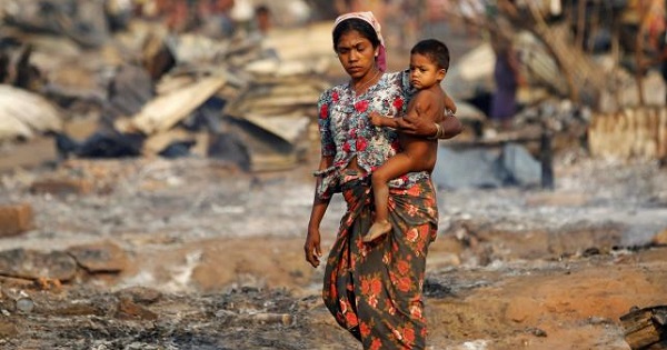 A woman carrying a baby walks among debris after fire destroyed shelters at a camp for internally displaced Rohingya Muslims in the western Rakhine State near Sittwe, Myanmar May 3, 2016.