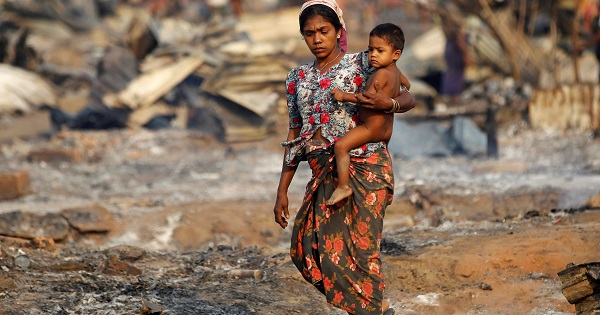A woman carrying a baby walks among debris after fire destroyed shelters at a camp for internally displaced Rohingya Muslims in the western Rakhine State in Myanmar, May 3, 2016.