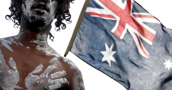 An Indigenuos Australian performer stands in front of an Australian flag