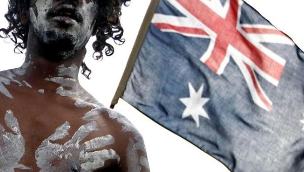 An Indigenuos Australian performer stands in front of an Australian flag