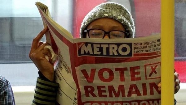 A woman reads a newspaper on the underground in London with a 