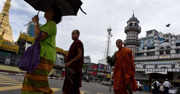 Two Buddhist monks cross the street intersection in front of Bengali Sunni Jameh mosque (right) in Yangon, on June 10, 2016.