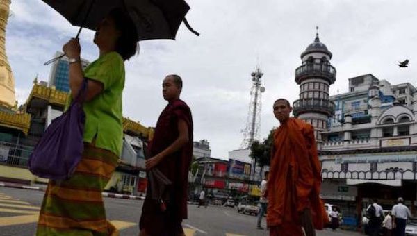 Two Buddhist monks cross the street intersection in front of Bengali Sunni Jameh mosque (right) in Yangon, on June 10, 2016.