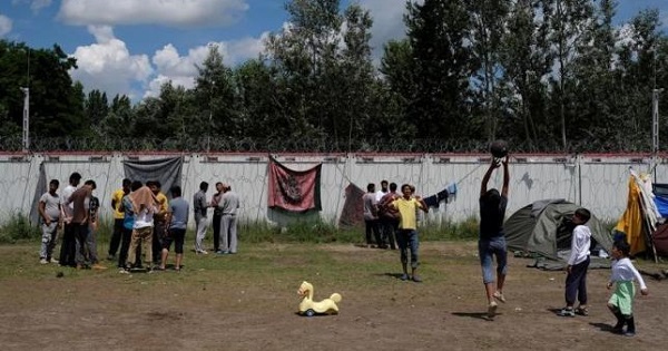 Migrants from Afghanistan stand by the Serbian-Hungarian border fence at a makeshift camp near the village of Horgos, Serbia, June 14, 2016.