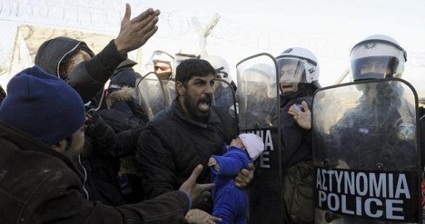 A stranded migrant holding a baby shouts next to a Greek police cordon following scuffles at the Greek-Macedonian border, near the village of Idomeni.