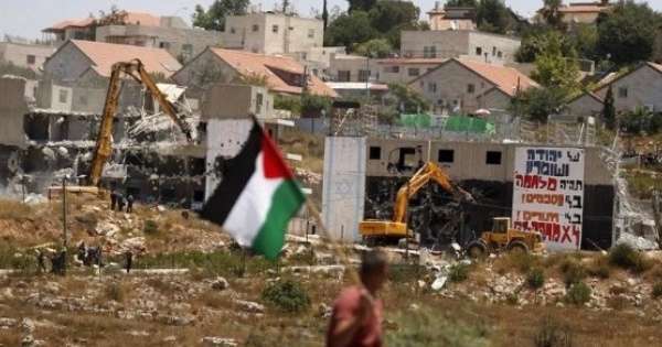 A Palestinian flag as Israeli heavy machinery demolish apartment blocs in the West Bank Jewish settlement of Beit El July 29, 2015