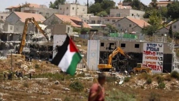 A Palestinian flag as Israeli heavy machinery demolish apartment blocs in the West Bank Jewish settlement of Beit El July 29, 2015