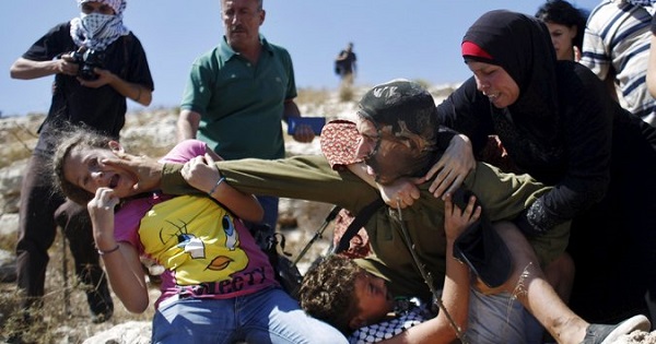 Palestinian protesters struggle with an Israeli soldier to prevent the arrest of a boy for throwing rocks.