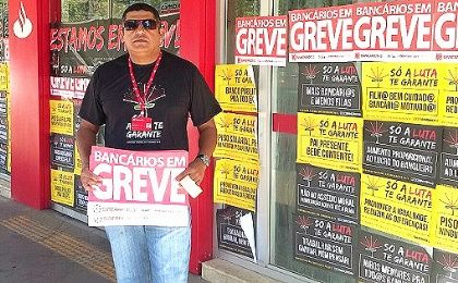 A worker stands in front of a bank in Brasilia plastered with signs saying 