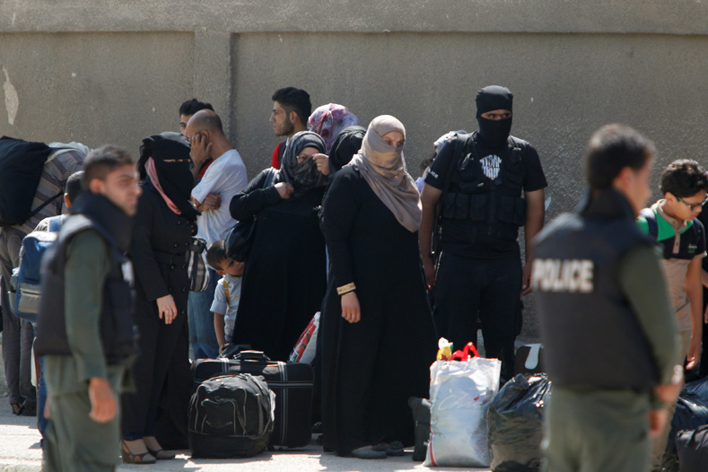 Syrian Army soldiers (foreground) stand guard as Syrian rebels and their families wait to ride a bus to evacuate the besieged Waer district in the central Syrian city of Homs, after a local agreement reached between rebels and Syria's army, Syria Sept. 22, 2016.