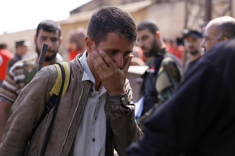 A rebel fighter reacts while walking next to Syrian Army soldiers prior to evacuating the besieged Waer district in the central Syrian city of Homs, after a local agreement reached between rebels and Syria's army, Syria Sept. 22, 2016.