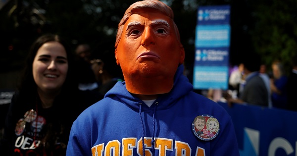 A man stands while wearing a mask depicting Republican nominee Donald Trump outside Hofstra University, Sept. 26, 2016.