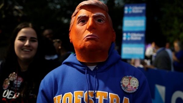 A man stands while wearing a mask depicting Republican nominee Donald Trump outside Hofstra University, Sept. 26, 2016.