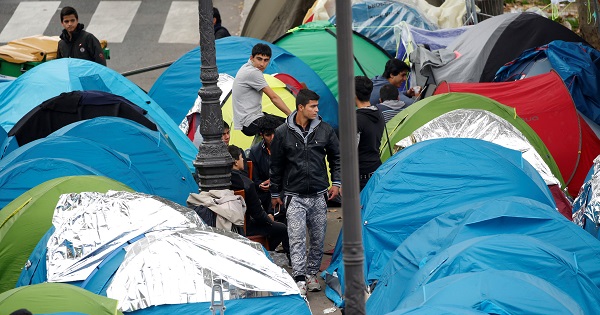 Refugees stand near their tents at a makeshift migrant camp on a street near the metro stations of Jaures and Stalingrad in Paris, France, Oct. 28, 2016.