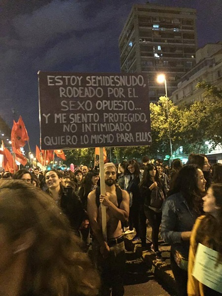 A man in a march in Chile stands with a sign that reads 