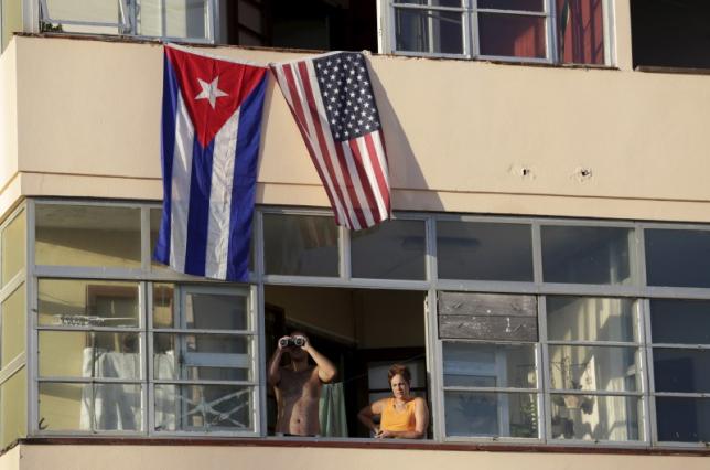 Cuban residents living next to the U.S. embassy look out of a window underneath the Cuban and U.S. flags in Havana, Aug. 14, 2015.