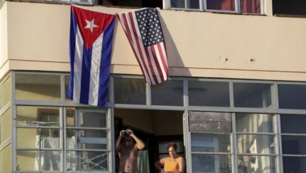 Cuban residents living next to the U.S. embassy look out of a window underneath the Cuban and U.S. flags in Havana, Aug. 14, 2015.