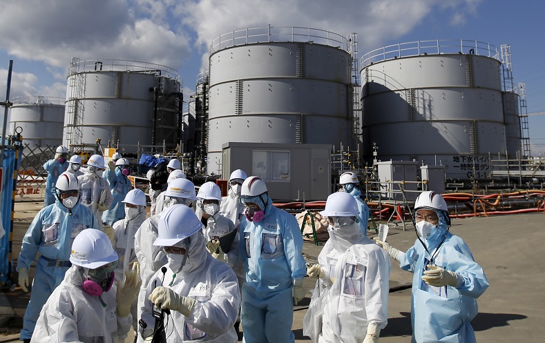 Members of the media, wearing protective suits and masks, walk after receiving a briefing from Tokyo Electric Power Co. (TEPCO) employees (in blue) in front of storage tanks for radioactive water at TEPCO's tsunami-crippled Fukushima Daiichi nuclear power plant in Okuma town,Fukushima prefecture, Japan in this Feb. 10, 2016 file photo. 