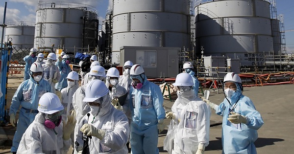 Members of the media, wearing protective suits and masks, walk after receiving a briefing from Tokyo Electric Power Co. (TEPCO) employees (in blue) in front of storage tanks for radioactive water at TEPCO's tsunami-crippled Fukushima Daiichi nuclear power plant in Okuma town,Fukushima prefecture, Japan Feb. 10, 2016.