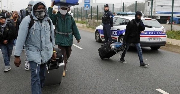 French police stand near as migrants carry their belongings at the start of their evacuation and transfer to reception centers in France, October 24, 2016.