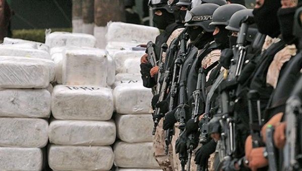 Mexican authorities stand guard beside seized narcotics.