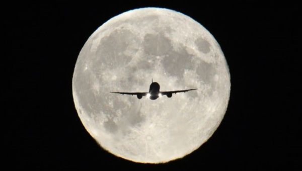 A plane flies in front of the moon.