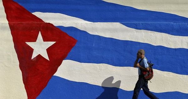 A man walks by a mural of the Cuban flag.