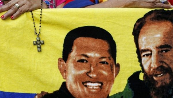 A supporter holds a crucifix next to a flag of Hugo Chavez (L) with Fidel Castro (R) in Caracas Jan. 5, 2013