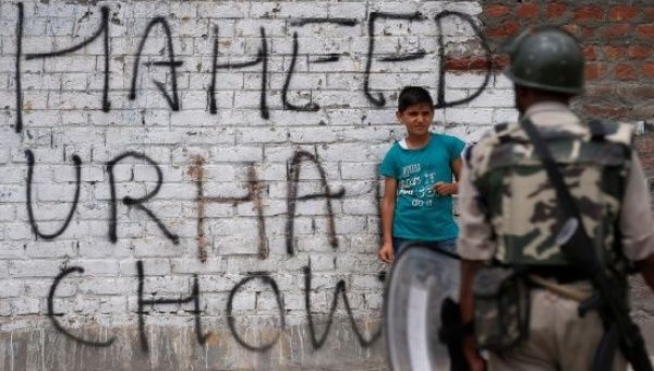 A boy stands next to a wall painted with graffiti as a policeman stands guard during a protest in Srinagar, Kashmir. 