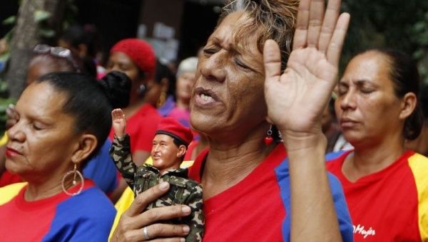 A supporter of Venezuela's Bolivarian Revolution prays as she holds a doll depicting former President Hugo Chavez.