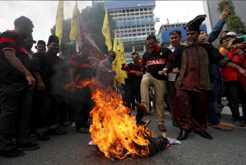 Pro-Palestine demonstrators watch as the smoldering remains of a Trump effigy burns in Kuala Lumpur, Malaysia amidst a rise of protests worldwide.