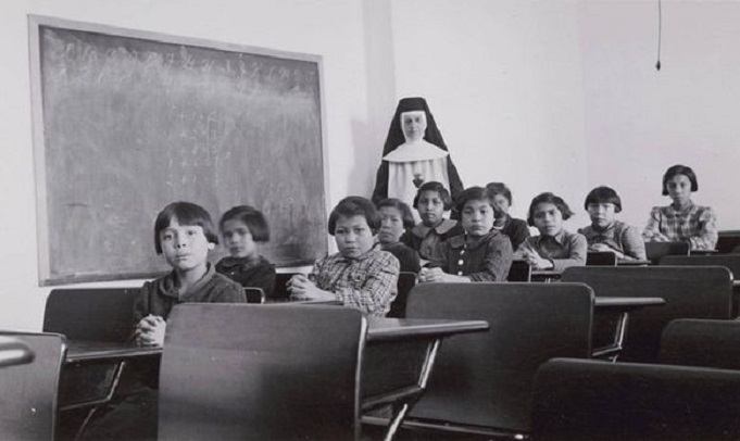 A group of female students and a nun pose in a classroom at Cross Lake Indian Residential School in Cross Lake, Mba., in a February, 1940.