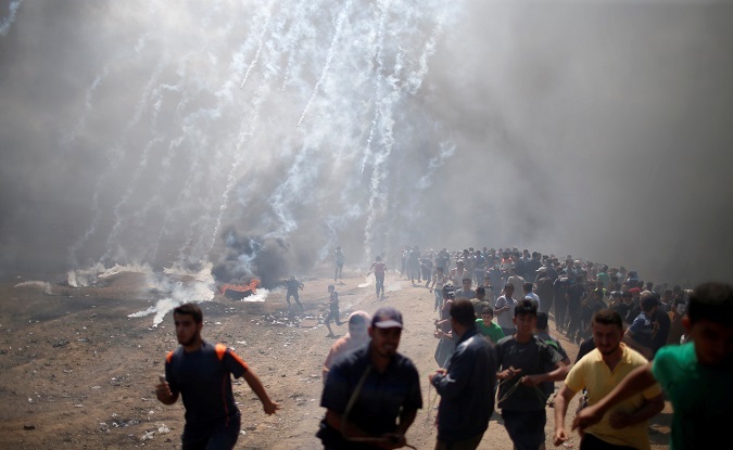 Palestinian demonstrators run from tear gas fired by Israeli troops during a protest against U.S. embassy move to Jerusalem and ahead of the 70th anniversary of Nakba, at the Israel-Gaza border east of Gaza City May 14, 2018. 