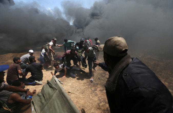 A wounded Palestinian demonstrator is evacuated as others take cover from Israeli fire and tear gas 