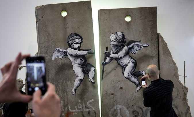Visitors take photographs of the 'replica separation barrier' created by British street artist Banksy as it stands on display at the Palestine tourist stand at the World Trade Fair at the Excel centre in London, UK Nov. 5, 2018.