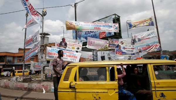 A man rides on the back of a vehicle near election banners in Kinshasa, Congo, Dec. 27, 2018.