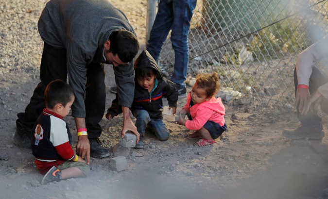 A man gives children rocks to play with inside an enclosure, where they are being held by U.S. Customs and Border Protection (CBP).
