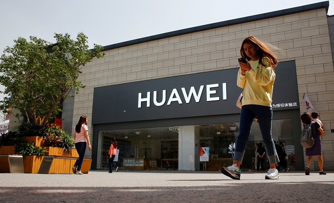 A woman looks at her phone as she walks past a Huawei shop in Beijing, China May 16, 2019.