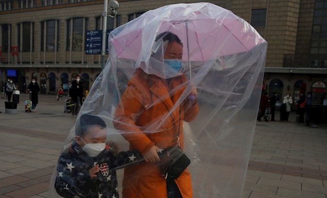 Woman covers herself and her chid's body as protection from Coronavirus at a railway station in Beijing, China, 11 Feb. 2020.