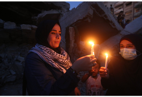 Palestinians hold candles near buildings destroyed in Israeli air strikes in the southern Gaza Strip city of Rafah, on May 25, 2021
