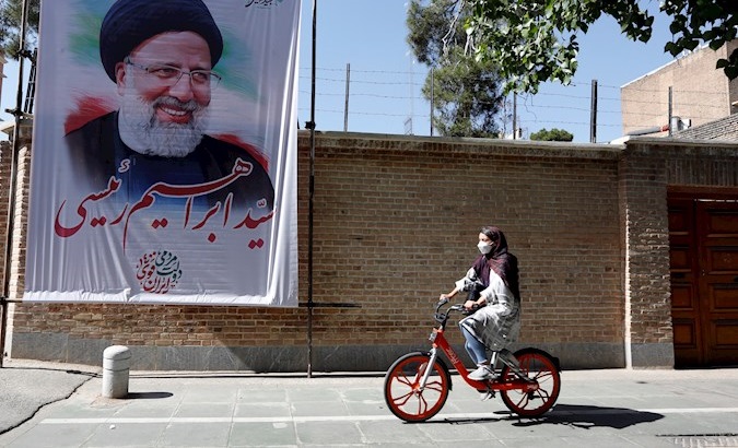 A girl rides a bicycle next to a poster depicting presidential candidate Ebrahim Raisi, Tehran, Iran, May 30, 2021.
