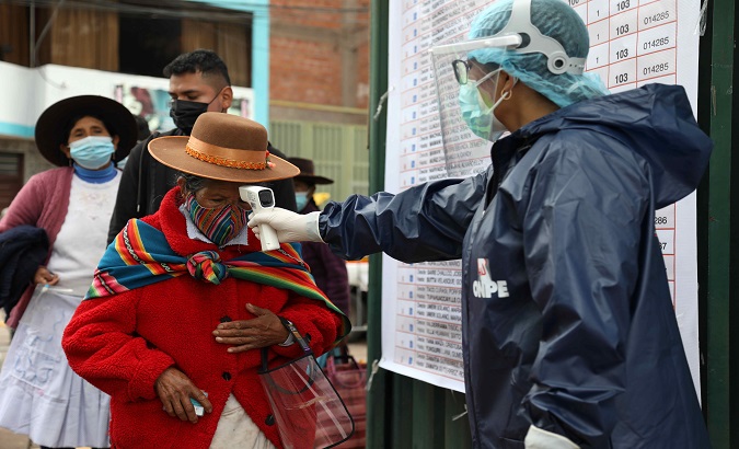 An election official measures the temperature of a woman entering a polling station, Cusco, Peru, April 11, 2021.