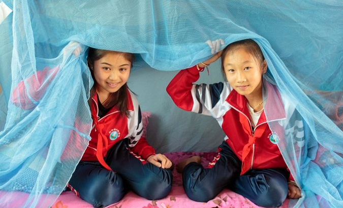 Chinese children inside a mosquito net tent.