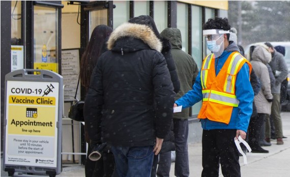 A staff member wearing face masks and a face shield helps people register outside a COVID-19 vaccine clinic in Mississauga, Ontario, Canada, on Jan. 22, 2022.