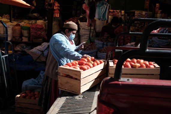 A vendor checks her cellphone as she unloads boxes of tomatoes from a truck in La Paz, Bolivia, on Aug. 18, 2022.