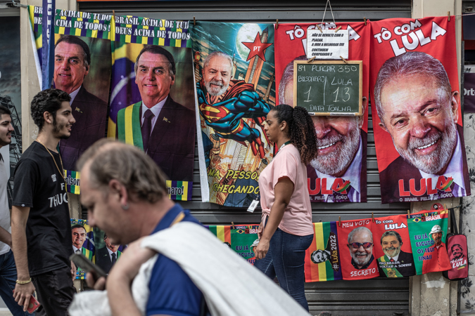 Several people walk in front of a street towel stall with images of the current president of Brazil and candidate for re-election, Jair Bolsonaro, and his contender, former Brazilian president Luiz Inácio Lula da Silva