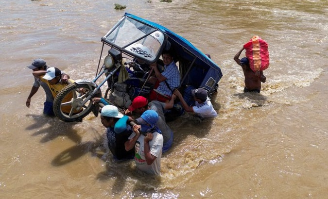 People push a motorcycle stuck in a flood.